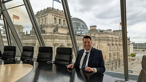 Foto zum Thema "Politikaktionswoche dbb jugend": Zu sehen ist Fabian Schütze. Er sitzt an einem Besprechungstisch, im Hintergrund der Reichstag.