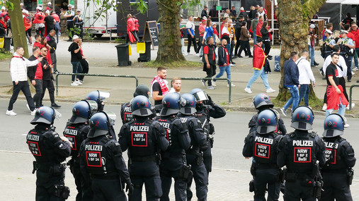 Reportage Einsatzversorgung - Bildergalerie Foto zum Thema "Polizei Einsatzversorgung": Zu sehen sind Polizist*innen in Schutzkleidung, die Fans beobachten.