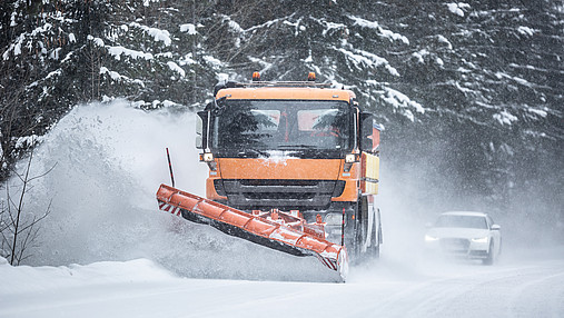 Ein Schneepflug des Straßenverkehrsdienstes räumt eine verschneite Straße.