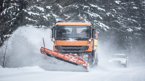 Ein Schneepflug des Straßenverkehrsdienstes räumt eine verschneite Straße.