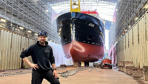 Foto zum Thema "Ausbildung zum Schiffsmechaniker": Zu sehen ist Tobias, der die Ausbildung absolviert hat, im Trockendock vor dem Schiff "Atair".
