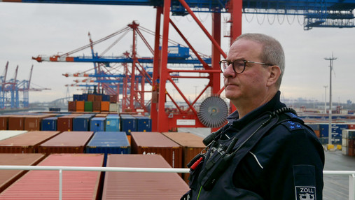 Foto zum Thema „Zoll Hamburger Hafen“: Zu sehen ist Felix, der an Deck des Containerschiffes über das Hafengelände schaut.