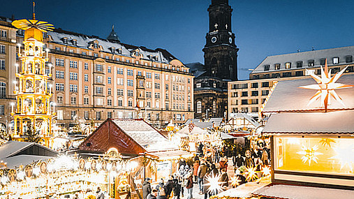 Foto zum Thema "Dresdner Striezelmarkt": Zu sehen ist der Markt, die Lichter leuchten in der Dunkelheit. Links im Bild ist die Weihnachtspyramide.