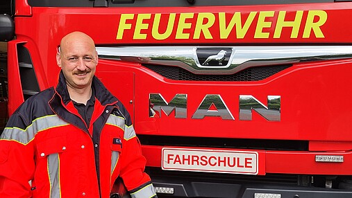 Foto zum Thema "Fahrschule Feuerwehr": Zu sehen ist Christoph, Fahrlehrer und Feuerwehrmann. Er steht vor einem Löschfahrzeug.