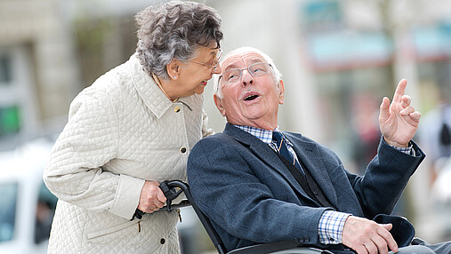 Foto zum Thema "Ausbildung bei der Sozialversicherung": Zu sehen ist ein Senioren-Pärchen. Er sitzt im Rollstuhl, sie schiebt.