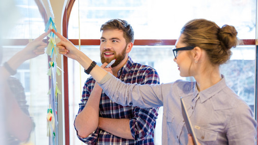 Foto zum Thema "was bedeutet agiles Arbeiten": Zu sehen sind ein Mann und eine Frau, die an einem Flipchart stehen. Sie schauen nachdenklich.