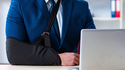 Ein Mann mit Armschlinge sitzt am Computer in seinem Büro.