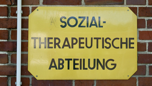 JVA Hahnöfersand - Sozialtherapie Foto zum Thema "JVA Hahnöfersand": Zu sehen ist ein Schild mit der Aufschrift "Sozialtherapeutische Abteilung", das an einer roten Backsteinmauer befestigt ist.