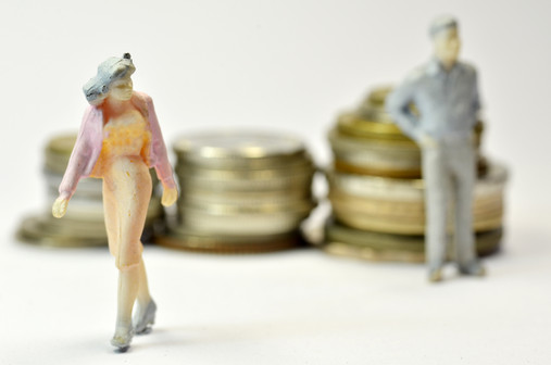 Miniaturfrau und Minaturmann vor einzelnen Stapeln mit Geldmünzen. Die Frau sieht so aus als ginge sie resigniert weg.