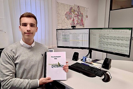 Foto zum Thema "wie wird man Kämmerer": Zu sehen ist Niklas Riedinger, Kämmerer der Gemeinde Forbach. Er sitzt am Schreibtisch und hält den Haushaltsplan in der Hand.